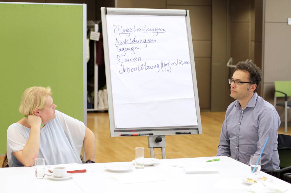 Monitoringstelle Dieses Foto zeigt zwei Personen an einem Tisch sitzen. Sie beratschlagen welche neuen Inhalte auf die Flipchart zu schreiben sind, die zwischen ihnen steht.